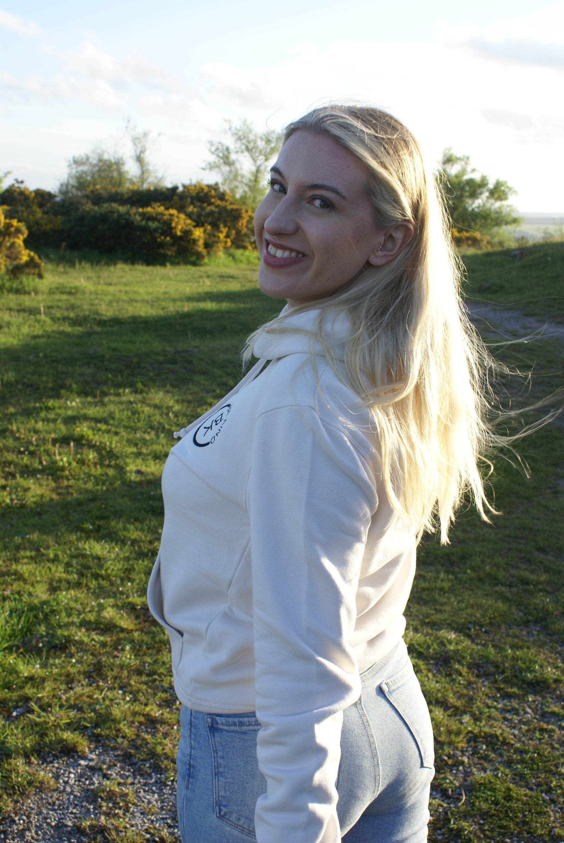 A woman stands in a windy field, she's wearing an Off White Organic Cotton Hoodie from the Be Kind Apparel Original Collection