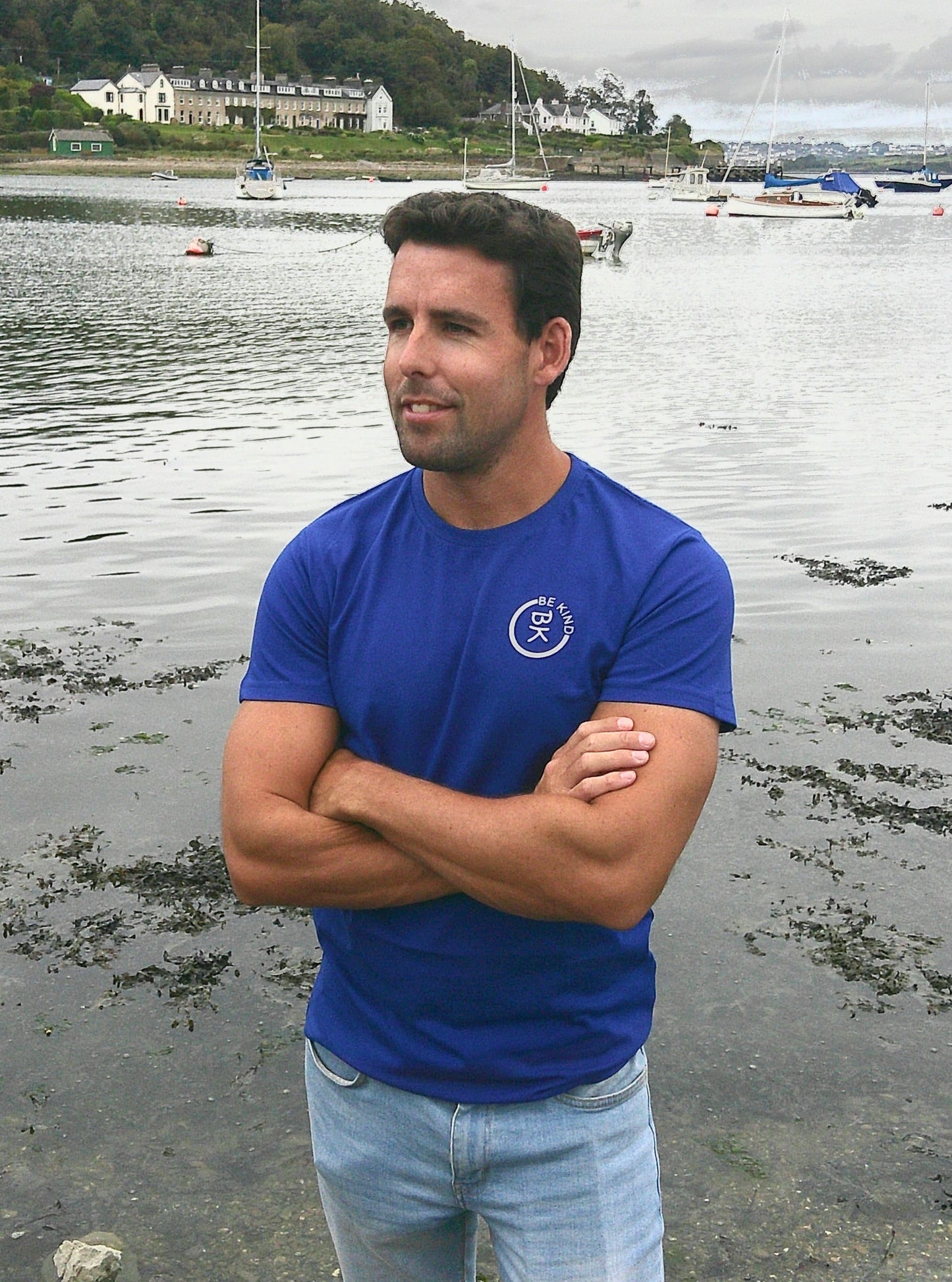 A man stands with folded arms, he's wearing a Cobalt Blue Organic Cotton Connector T-Shirt from the Be Kind Apparel Connector Range