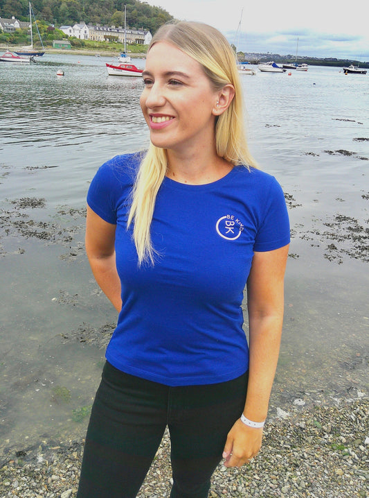 A woman stands by the shore, she's wearing a Cobalt Blue Organic Cotton Connector T-Shirt from the Be Kind Apparel Connector Range
