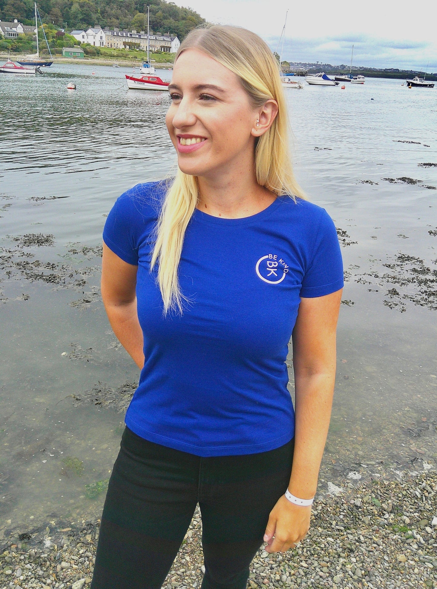 A woman stands by the shore, she's wearing a Cobalt Blue Organic Cotton Connector T-Shirt from the Be Kind Apparel Connector Range