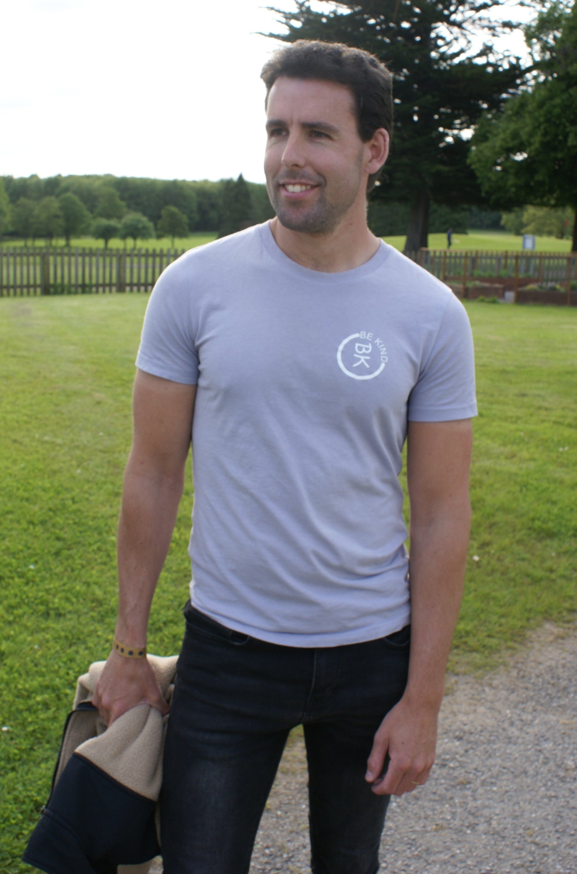 A man stands, he's wearing a Lavender Organic Cotton T-Shirt from the Be Kind Apparel Original Collection