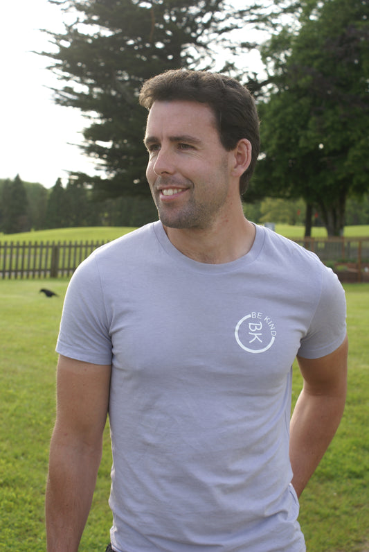 A man stands in a field, he's wearing a Lavender Organic Cotton T-Shirt from the Be Kind Apparel Original Collection