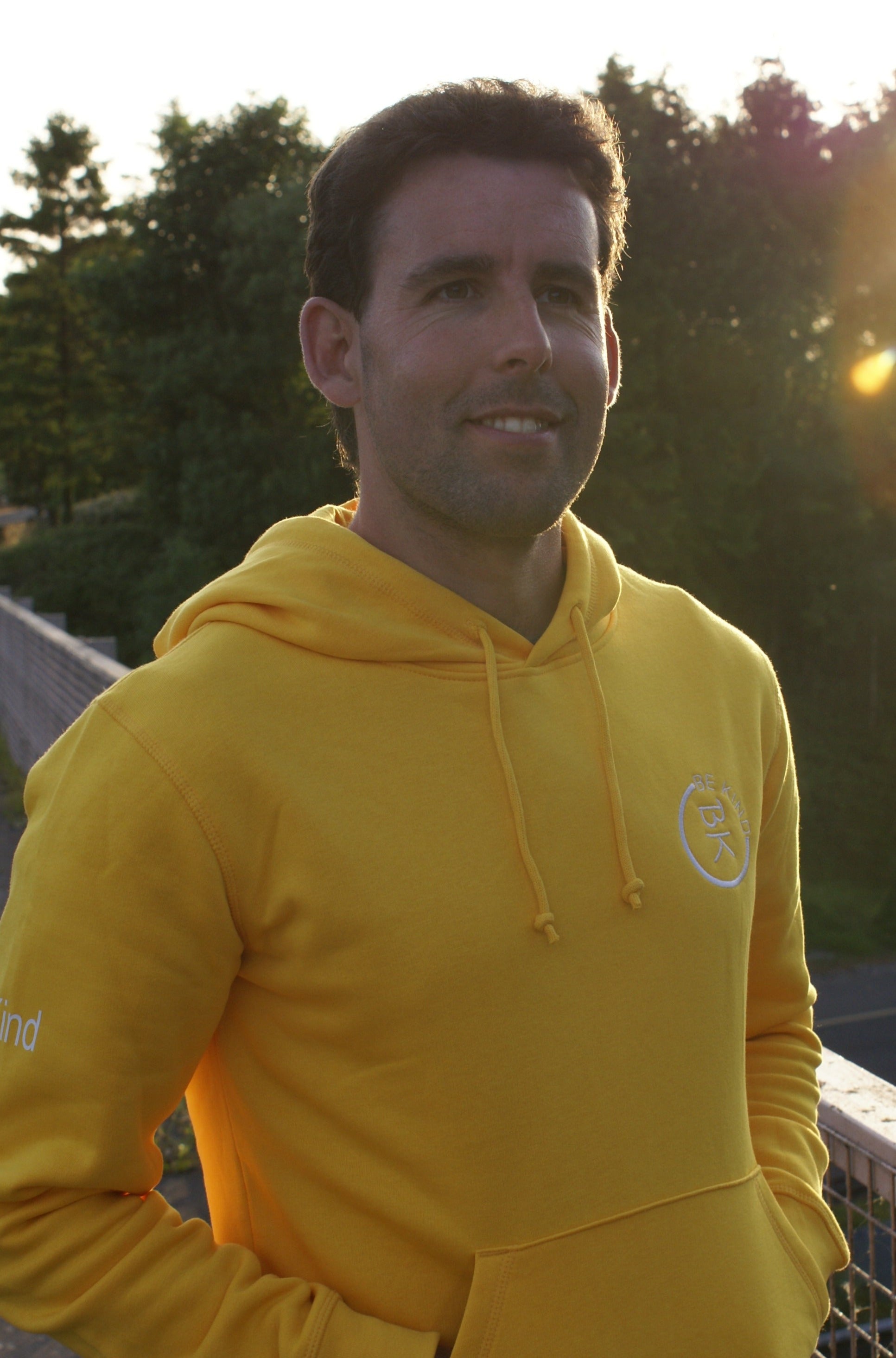 A man smiles, he's wearing a Sunshine Yellow Organic Cotton Hoodie from the Be Kind Apparel Original Collection