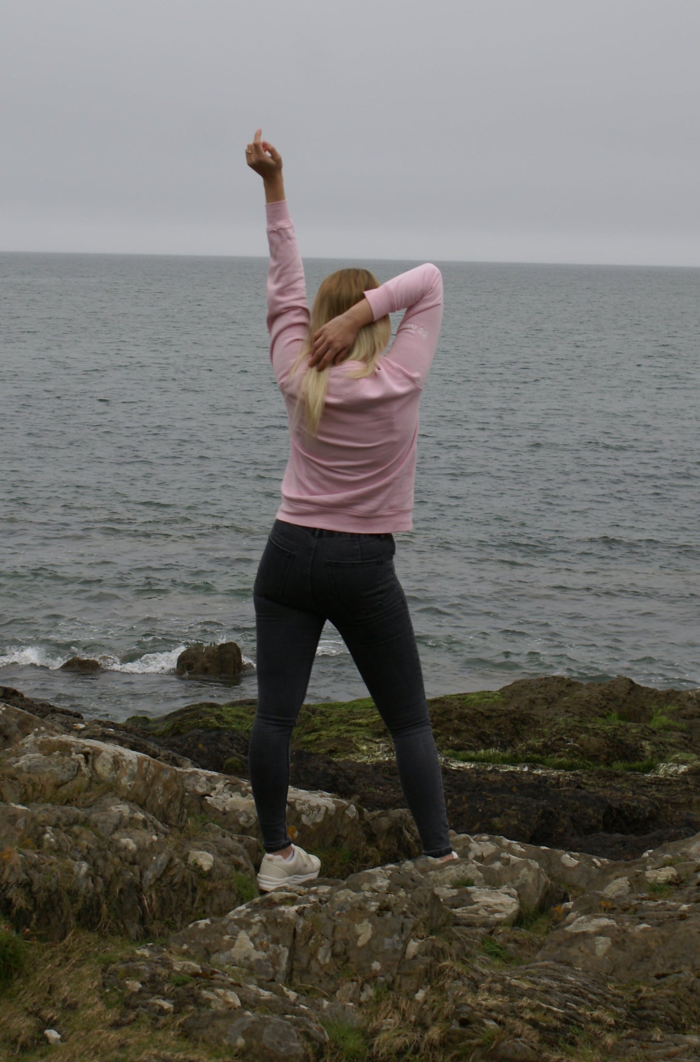 A woman struts a pose, she's wearing a Bubblegum Pink Organic Cotton Sweatshirt from the Be Kind Apparel Original Collection