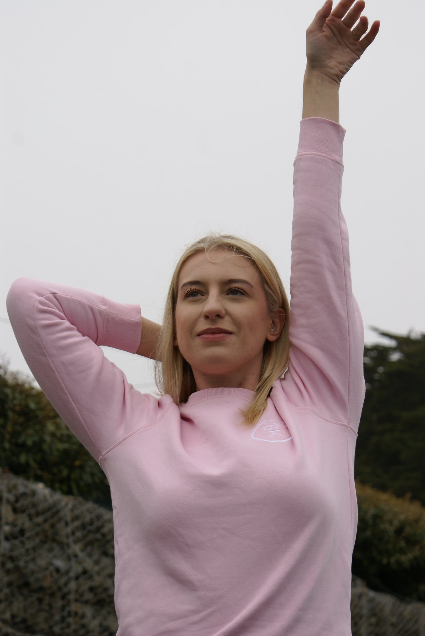 A woman looks at peace, she's wearing a Bubblegum Pink Organic Cotton Sweatshirt from the Be Kind Apparel Original Collection