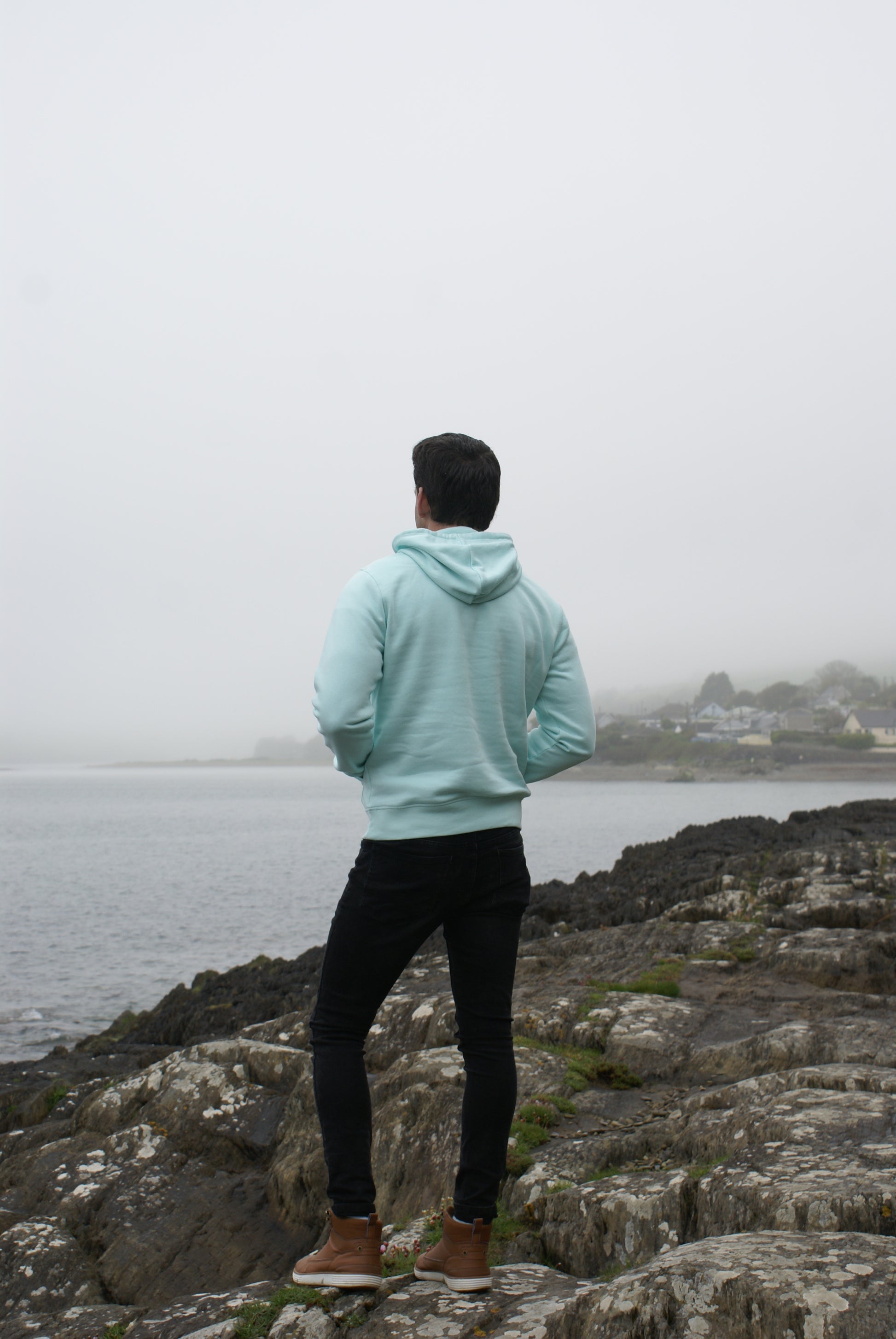 A man stands on rocks, he's wearing a Mint Green Organic Cotton Hoodie from the Be Kind Apparel Original Collection