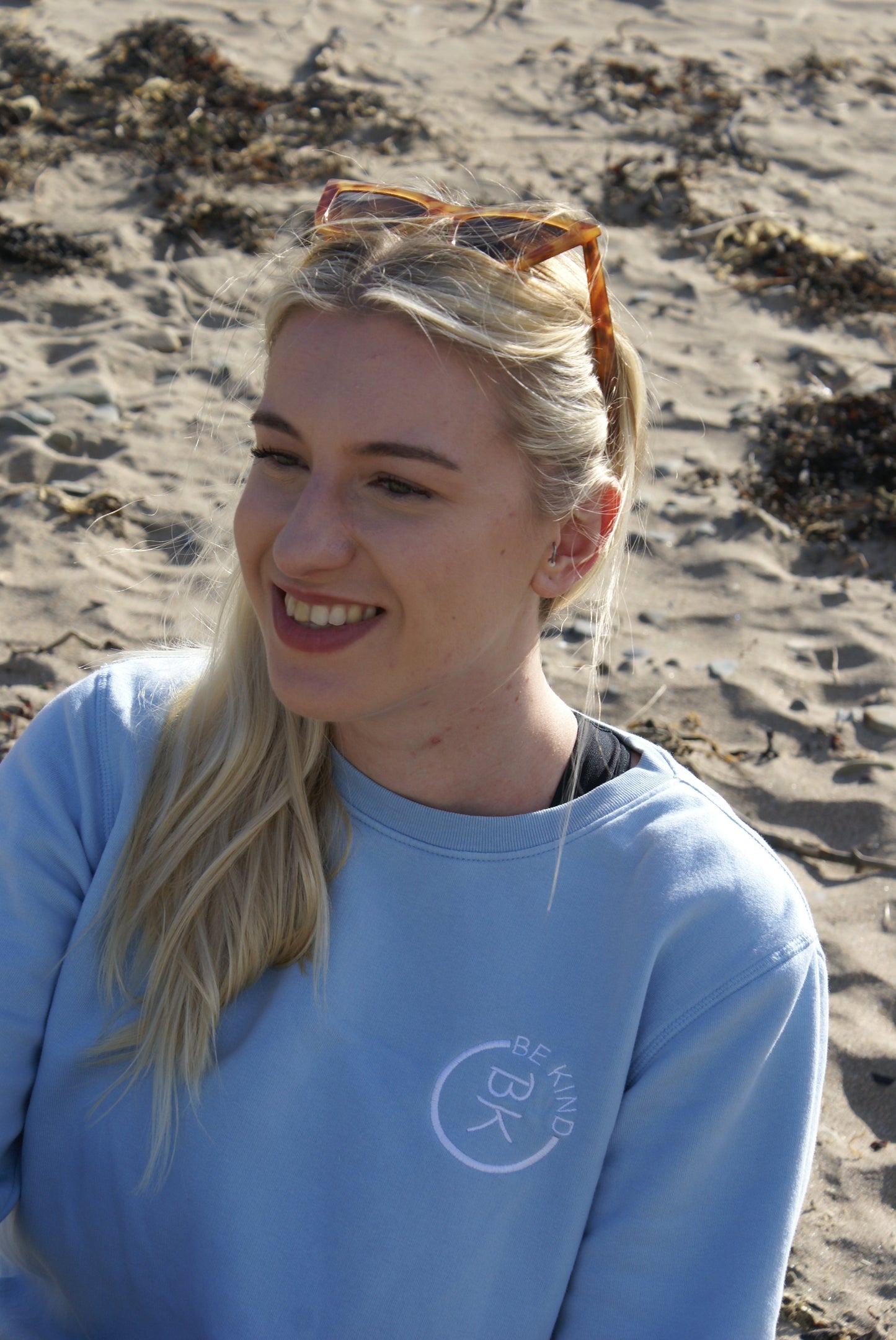 A woman smiles, she's wearing a Sky Blue Organic Cotton Sweatshirt from the Be Kind Apparel Original Collection