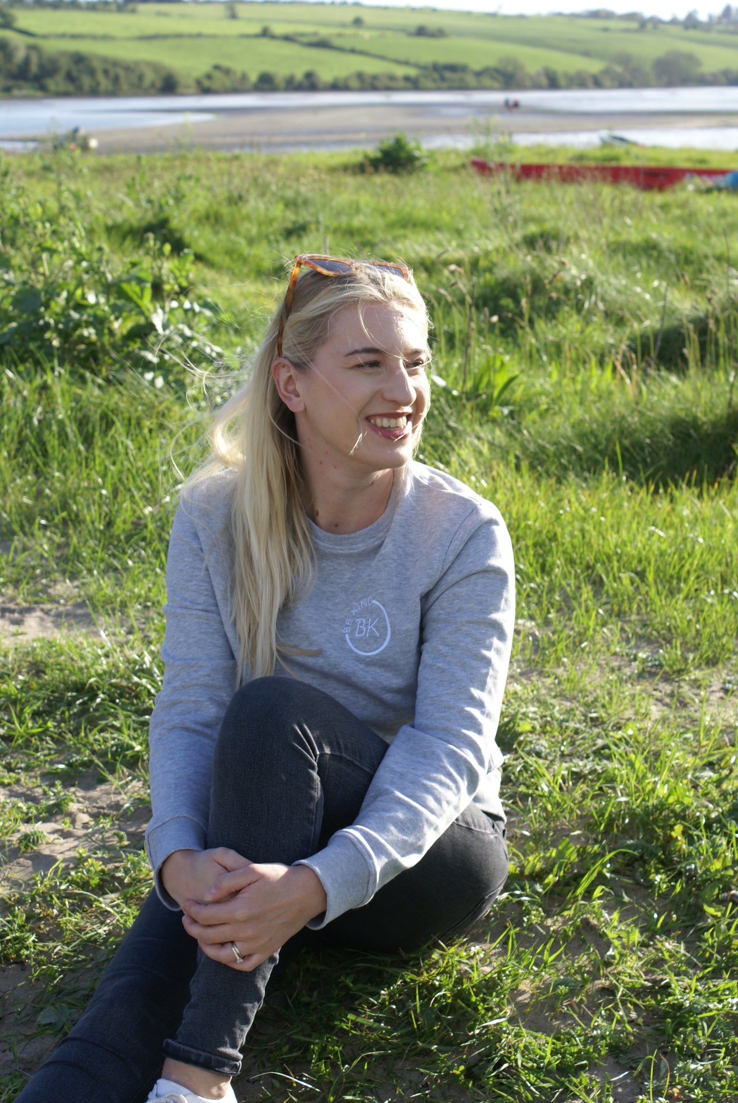 A woman sits in the grass, she's wearing a Grey Organic Cotton sweatshirt from Be Kind Apparel's Freestyle Range