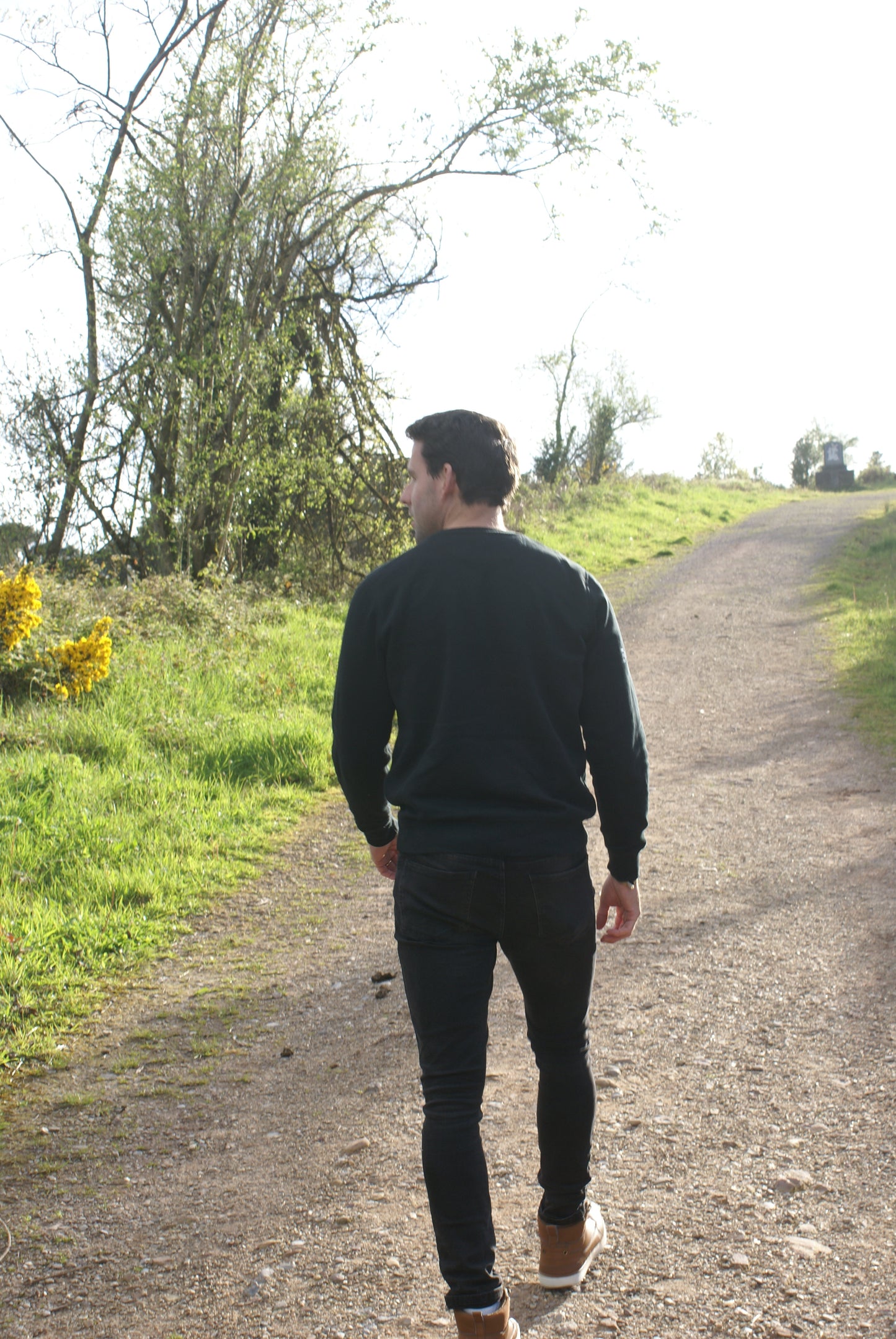 A man walks up a hill, he's wearing a Black Organic Cotton Sweatshirt from the Be Kind Apparel Original Collection