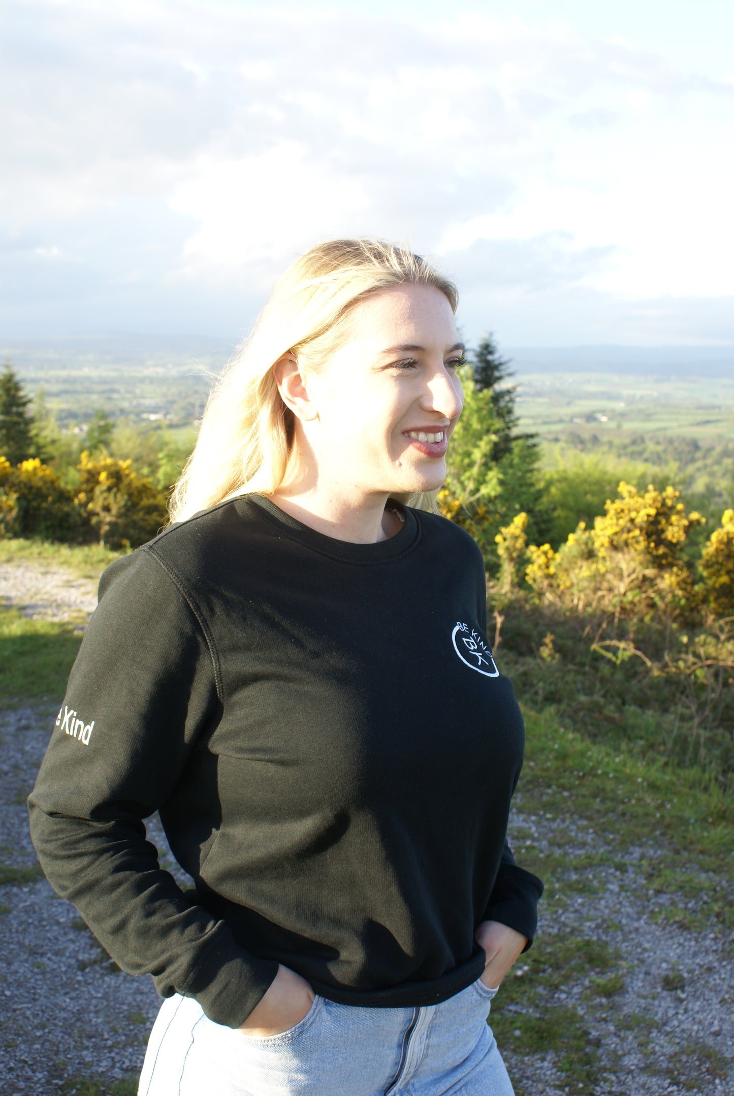 A woman smiles, she's wearing a Black Organic Cotton Sweatshirt from the Be Kind Apparel Original Collection