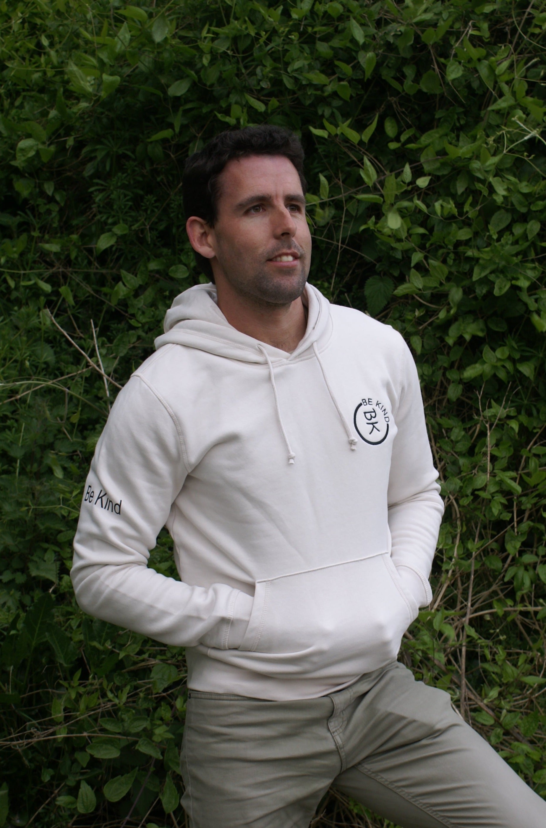 A man stands, he's wearing an Off White Organic Cotton Hoodie from the Be Kind Apparel Original Collection