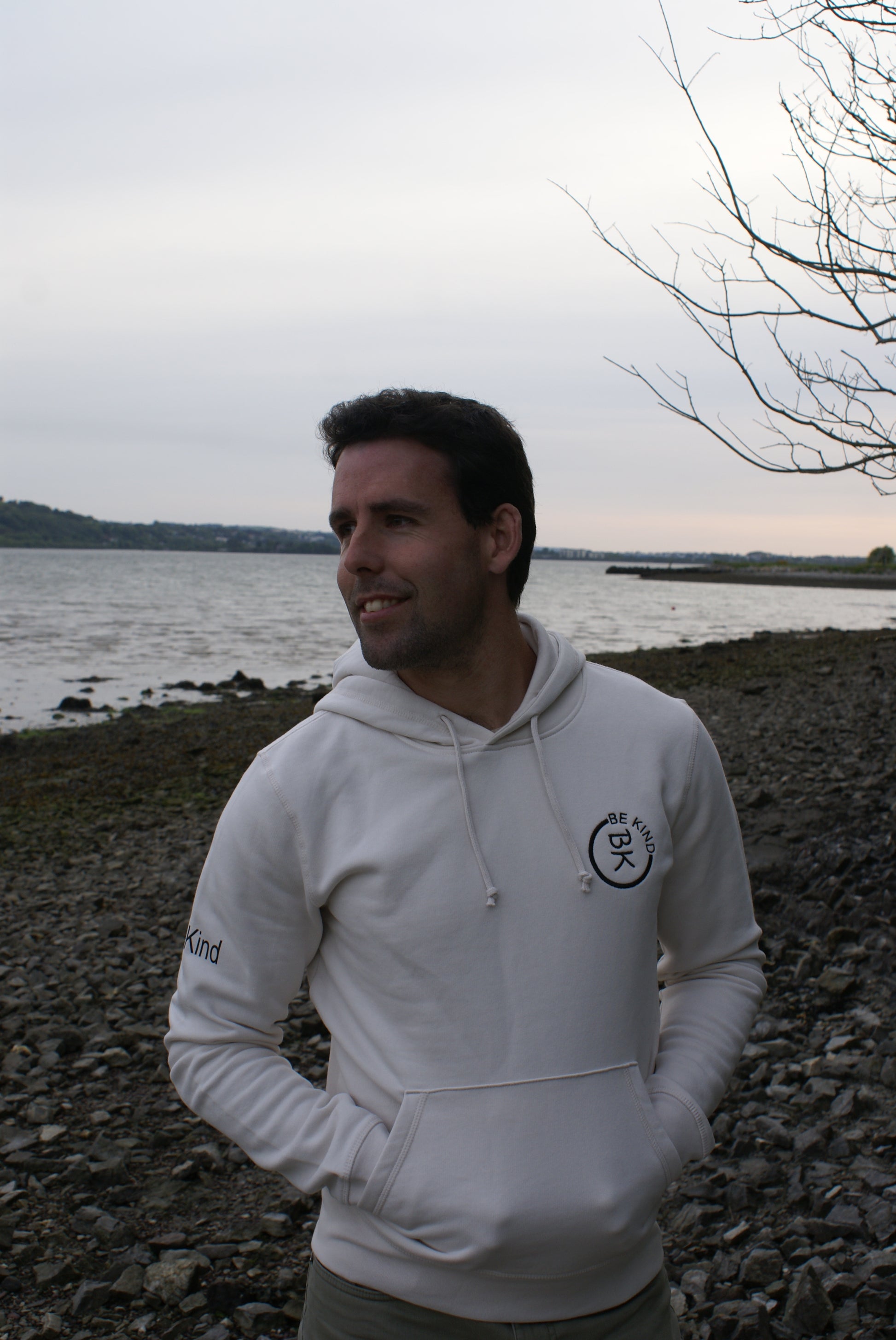 A man looks back, he's wearing an Off White Organic Cotton Hoodie from the Be Kind Apparel Original Collection