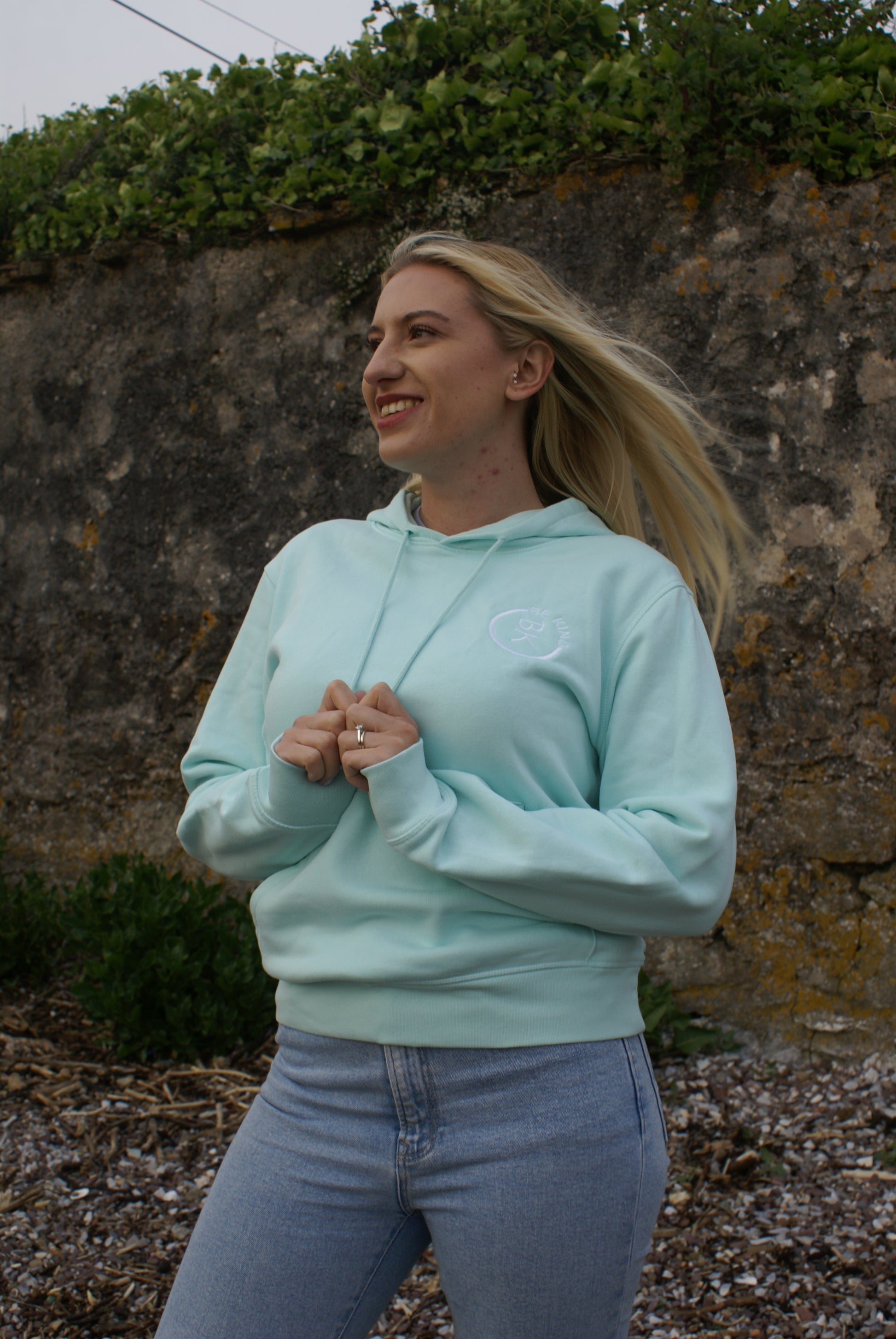 A woman stands in the wind, she's wearing a Mint Green Organic Cotton Hoodie from the Be Kind Apparel Original Collection