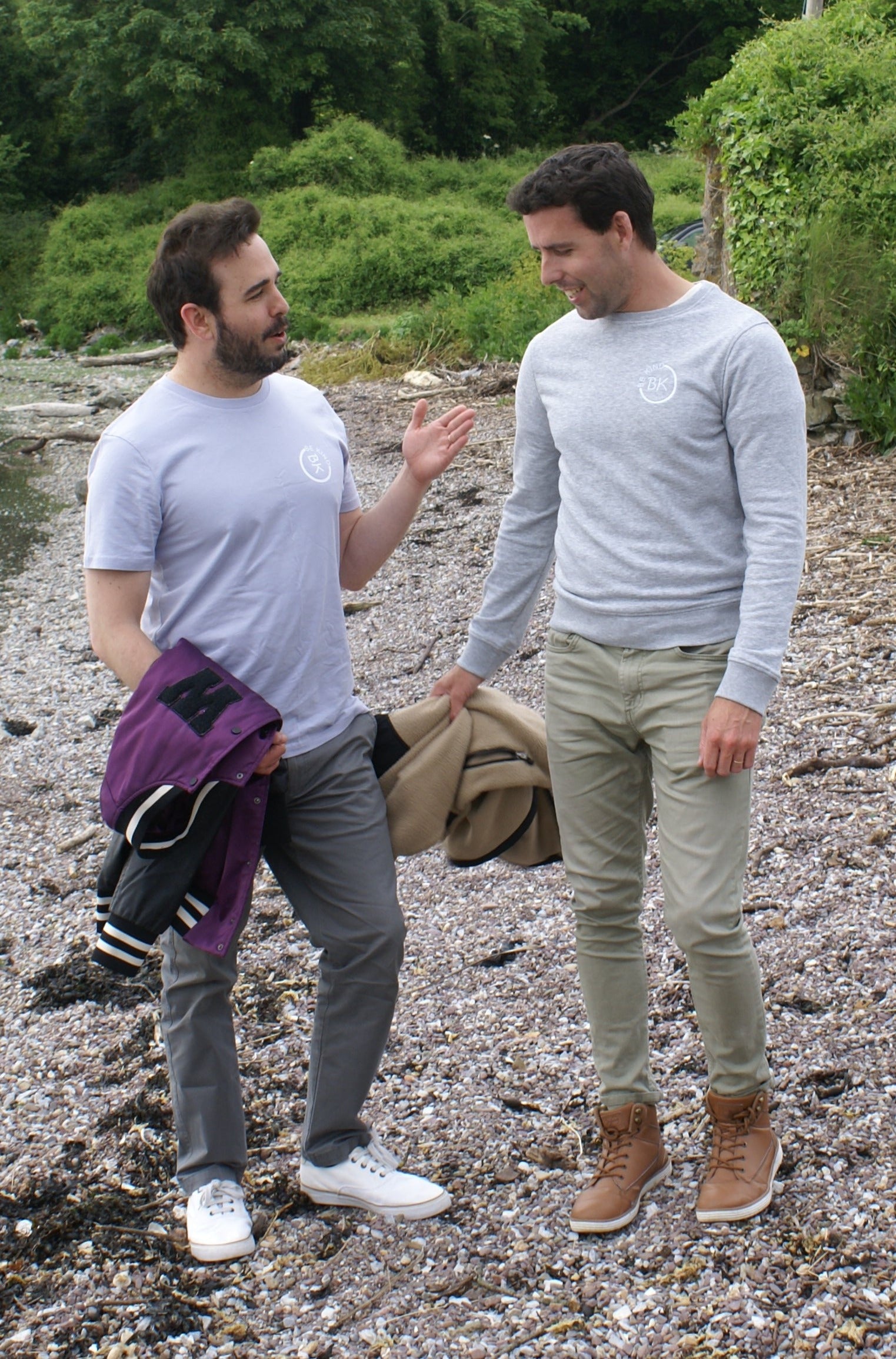 A man talks to another man on a beach, he's wearing a Grey Organic Cotton sweatshirt from Be Kind Apparel's Freestyle Range