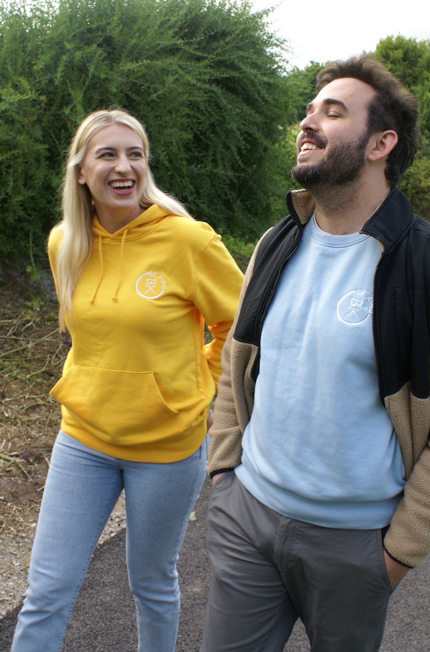 A woman laughs with a man, she's wearing a Sunshine Yellow Organic Cotton Hoodie from the Be Kind Apparel Original Collection