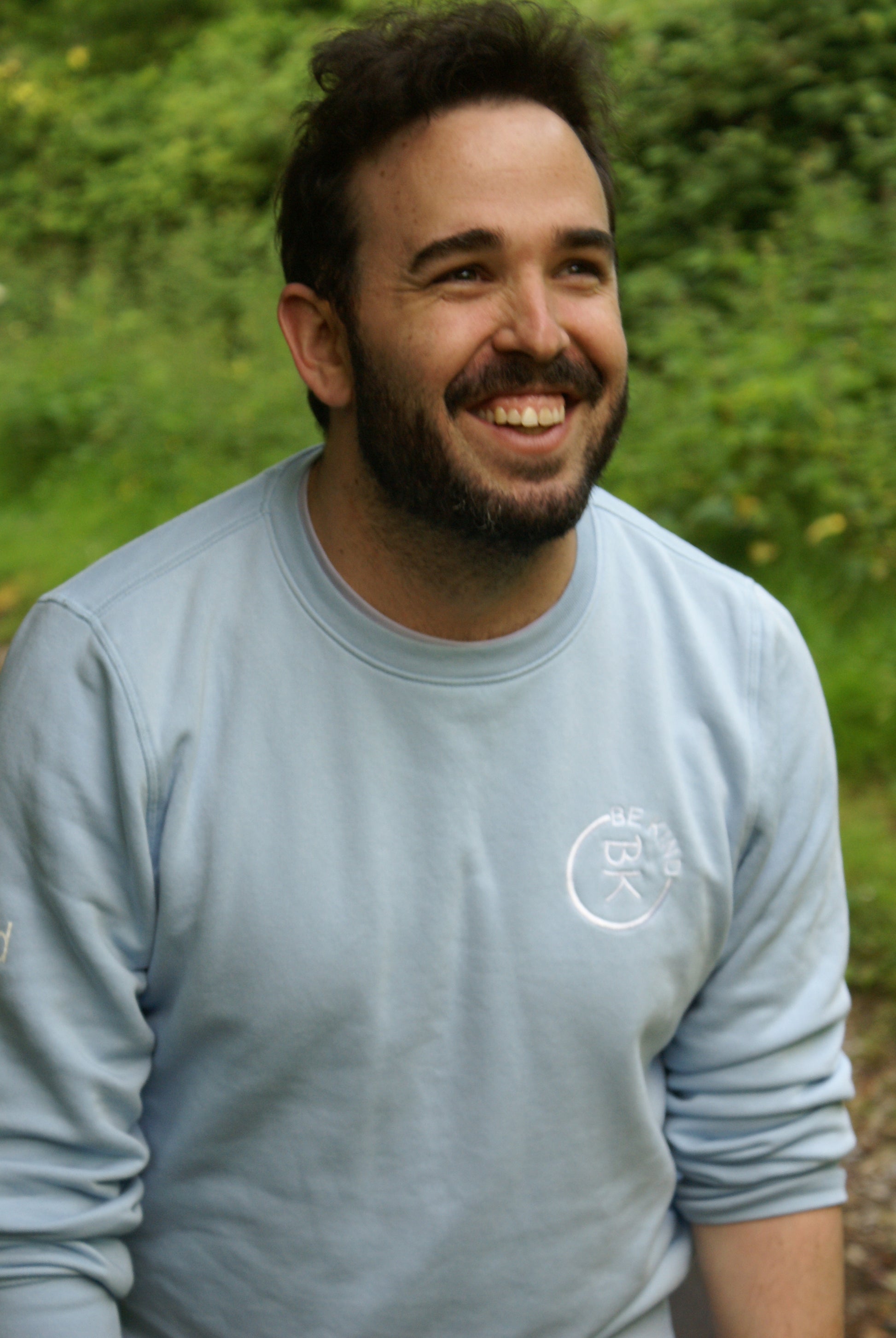 A man laughs,  he's wearing a Sky Blue Organic Cotton Sweatshirt from the Be Kind Apparel Original Collection