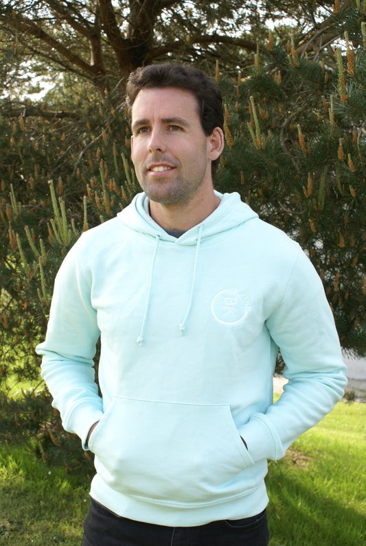 A man stands in a field, he's wearing a Mint Green Organic Cotton Hoodie from the Be Kind Apparel Original Collection