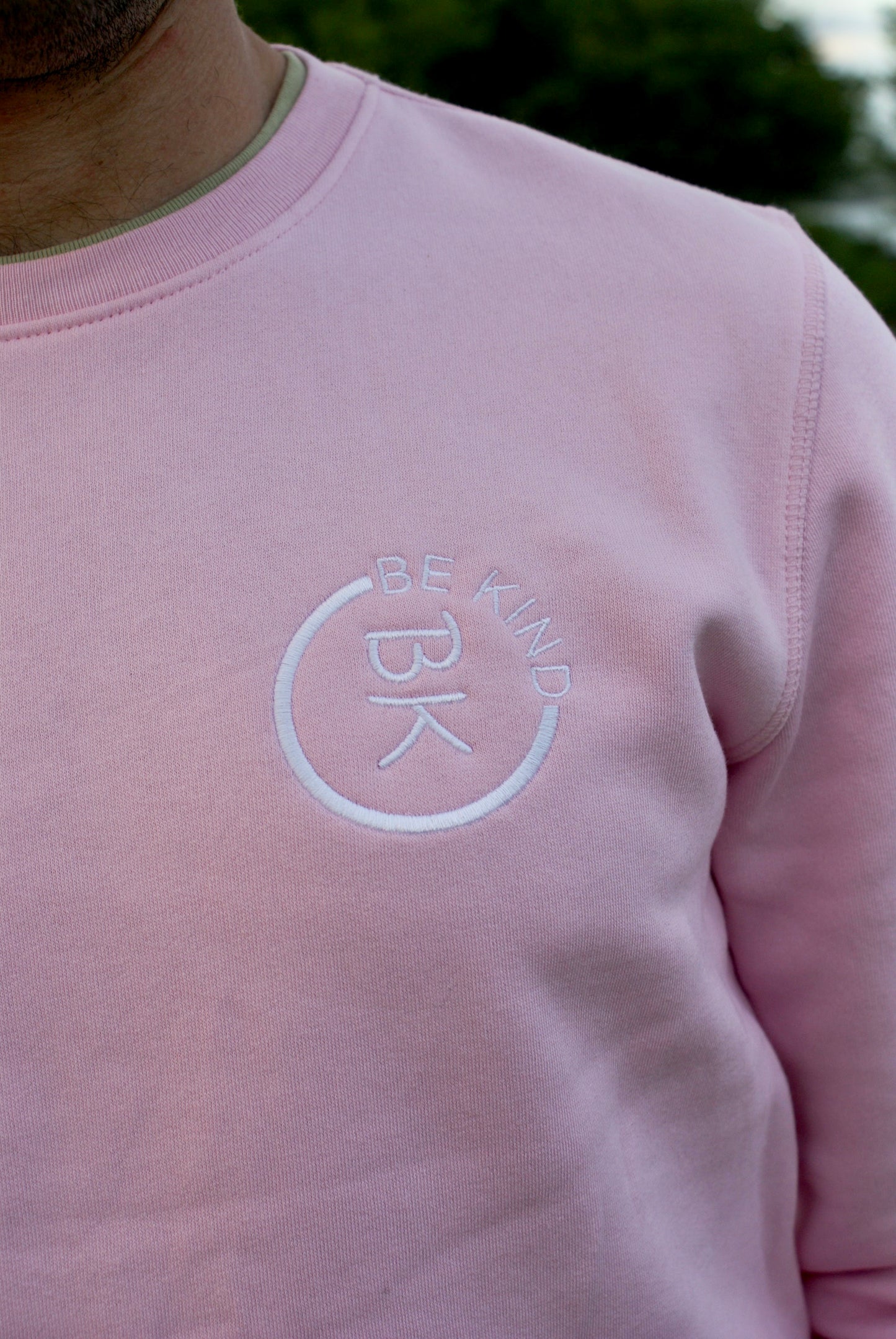 A man stands looking forward, he's wearing a Bubblegum Pink Organic Cotton Sweatshirt from the Be Kind Apparel Original Collection